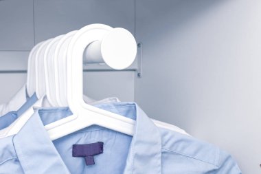 Mavi ve beyaz klasik erkek gömlekleri bir gardıropta askıda asılı.