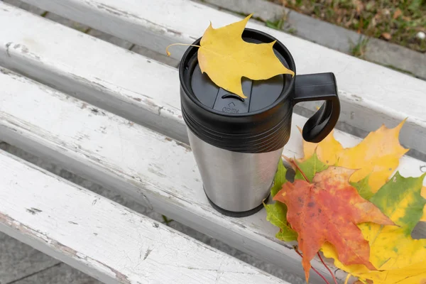 Сезон, осенние горячие напитки и концепция пикника - металлический термокофейный стакан в окружении красочных желтых листьев — стоковое фото