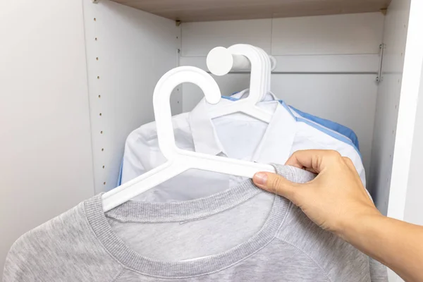 Woman hand choosing and taking gray casual sweatshirt in wardrobe fool of classic blue and white shirts, hanging on a rack — Stock Photo, Image