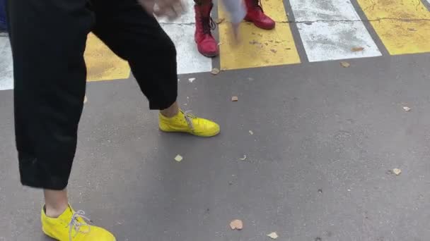 Pernas e pés de palhaços vestindo botas amarelas e vermelhas engraçadas coloridas, brincando uns com os outros na estrada de asfalto — Vídeo de Stock