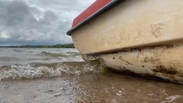 Ein im Hafen verankertes Boot, Dock in der Nähe des Wassers und Wellen, die gegen das Ufer und die Bootsseiten schlagen, niedriger Winkel — Stockvideo