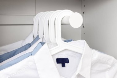 Mavi ve beyaz klasik erkek gömlekleri bir gardıropta askıda asılı.