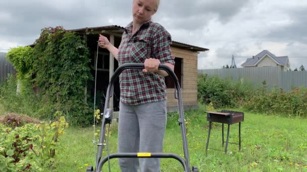 Mujer rubia tratando de arrancar el motor de una cortadora de césped, el trabajo de verano en el jardín, el corte de hierba verde — Vídeos de Stock