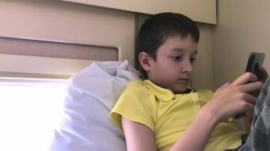Trende giden bir çocuk, tren kompartımanındaki bir yatakta uzanıyor ve akıllı telefon, toplu taşıma kablosuz internet kavramı kullanıyor.