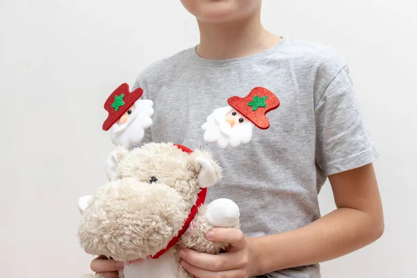 Мальчик с мягкой игрушкой, плюшевый бегемот с новогодними аксессуарами, карнавальный костюм с игрушечными елками на белом фоне - концепция детской вечеринки — стоковое фото