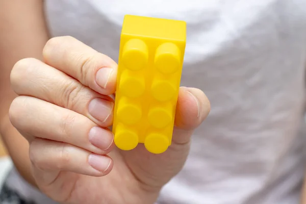 Woman holding colorful yellow toy plastic bricks, blocks for building, playing games and entertainment concept