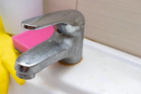Чистящие средства, перчатки и губка для мытья грязного крана с лимескалем, кальцинированный водопроводный кран с лаймовой шкалой на раковине в ванной комнате — стоковое фото