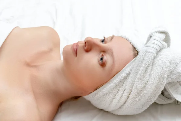 Спа уход за кожей красоты женщина с завернутыми волосами полотенце на голове после косметического лечения, белая женщина лежит на белом листе — стоковое фото