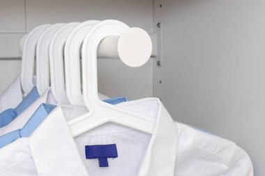 Mavi ve beyaz klasik erkek gömlekleri bir gardıropta askıda asılı.