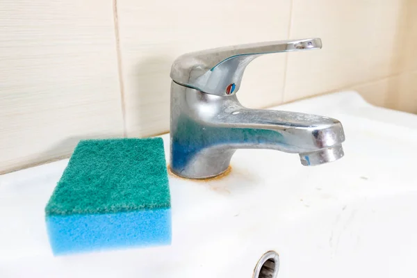 Niebieska gąbka do mycia brudnego kranu z wapnem, wapienny kran z wapnem na umywalce w łazience, koncepcja sprzątania domu — Zdjęcie stockowe