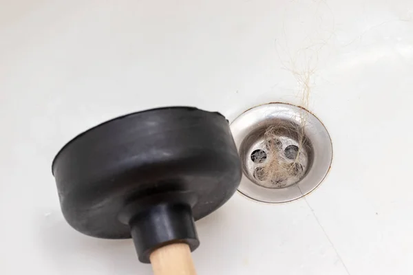 Blocked sewer, clogged bath drain with fallen out hair and a plunger near, hair loss in a bathroom