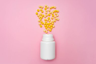 Sarı yuvarlak C vitamini, beyaz plastik şişenin yanında askorbik asit, pembe arka planda konteynır.