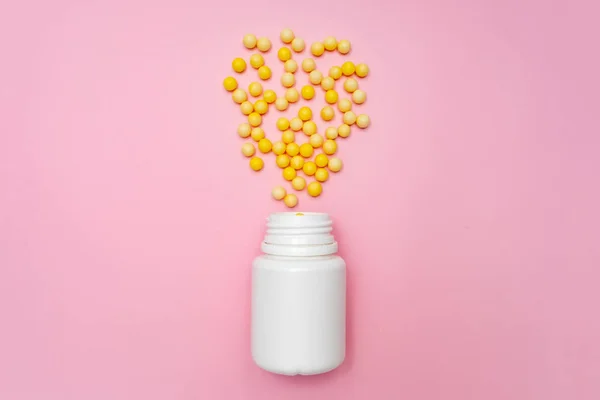 Amarelo dragees redondos de vitamina c, ácido ascórbico perto de uma garrafa de plástico branco, recipiente em fundo rosa — Fotografia de Stock