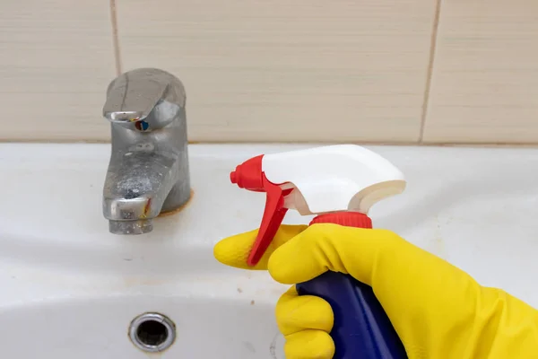 Ręcznie w żółtych gumowych rękawiczkach z rozpylanym środkiem czyszczącym do mycia brudnych kranów wapnem, zwapniałym kranem z wapnem na umywalce w łazience, koncepcja sprzątania domu — Zdjęcie stockowe