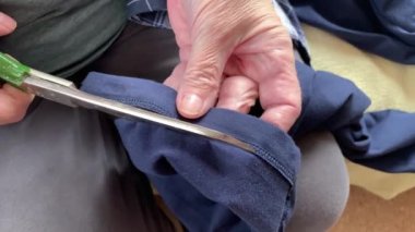 Yaşlı yaşlı bir kadın. Büyük bir makasla kumaş kesiyor. Elleri yakın.