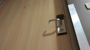 Bir kadın, elektronik güvenlik kilidine giriş kartı takarak bir otel odasının kapısını açıyor, kapıyı açıyor ve odaya giriyor.
