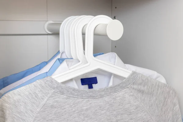 하얀 플라스틱 옷걸이에 걸려 있는 평범 한 면 스웨터와 전통적 인 셔츠는 파스텔 색상의 의상을 입고 있다 — 스톡 사진