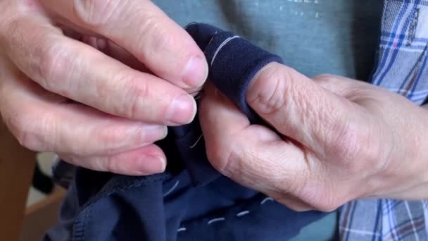 Старша літня жінка бабуся шиє тканинний одяг голкою, руки крупним планом — стокове відео