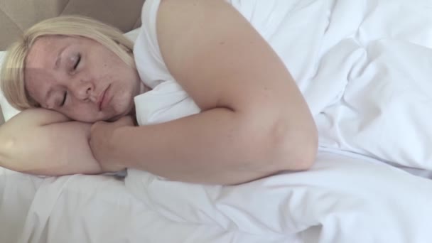 Slaperige vrouw van middelbare leeftijd liggend in bed en proberen wakker te worden door wrijven haar ogen en gezicht — Stockvideo