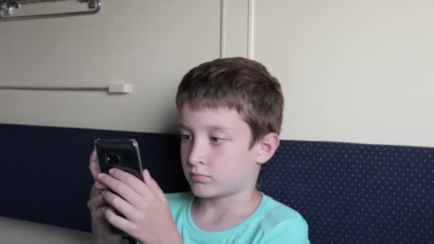 A preteen boy playing games on smartphone while riding in a train, travelling and journey — 비디오