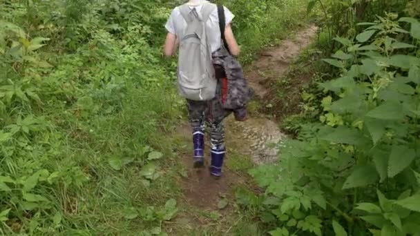 Egy turista sétál az erdei ösvényen, átkel a patakon, tavasszal, egy tinédzser fiú hátizsákkal az erdőben, túrázik. — Stock videók