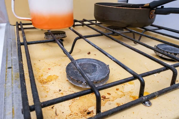 Dirty unhygienic surface of kitchen gas stove with grease and soot stains with kitchenware pans on it