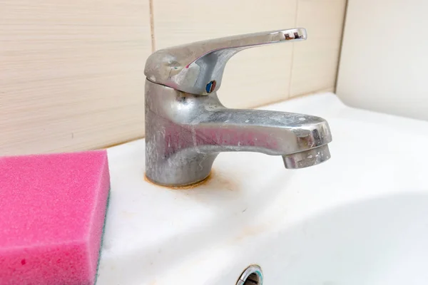 Esponja para lavar el grifo sucio con cal, grifo de agua calcificada con escala de cal en el lavabo en el baño, concepto de limpieza de la casa — Foto de Stock