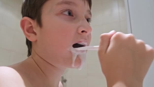 A portrait of a caucasian teen boy brushing teeth in bathroom, close up — Stockvideo