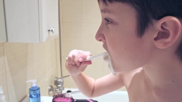 Портрет белого мальчика-подростка, чистящего зубы в ванной, крупным планом — стоковое видео