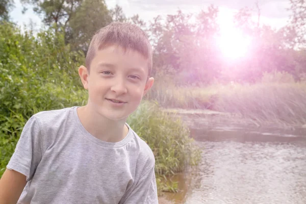 Портрет счастливого улыбающегося мальчика на открытом воздухе летом, зеленая природа и солнечный свет на заднем плане — стоковое фото