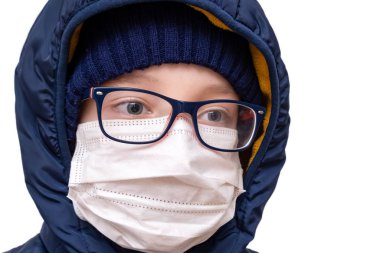 Koronavirüs karantinası kavramı. Virüs ve bakterilerden korunmak için kışlık giysiler ve beyaz solunum maskesi takan bir çocuk.