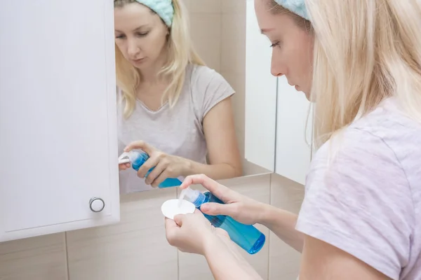 Mujer que usa gel micelar para limpiar su cara con una almohadilla de algodón, eliminando la suciedad y el maquillaje de la cara — Foto de Stock