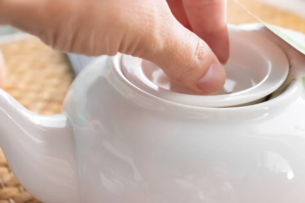 Женская рука, открывающая крышку керамического горшка с заваренным традиционным чаем в ресторане — стоковое фото