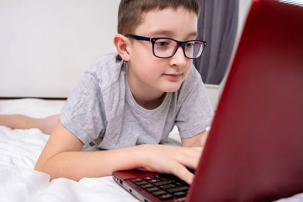 Um menino pré-adolescente deitado em uma cama, navegando na internet e digitando em seu blog, conceito de blog infantil — Fotografia de Stock