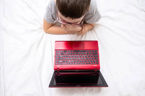 Un niño preadolescente acostado en una cama, navegando por Internet y escribiendo en su blog, concepto de blogueo infantil —  Fotos de Stock