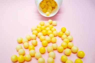 Sarı yuvarlak C vitamini, beyaz plastik şişenin yanında askorbik asit, pembe arka planda konteynır.