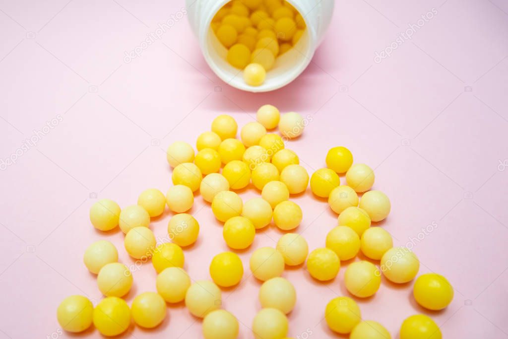 Yellow round dragees of vitamin c, ascorbic acid near a white plastic bottle, container on pink background