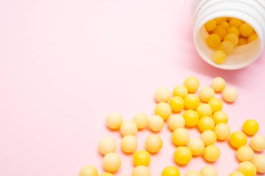 Sarı yuvarlak C vitamini, beyaz plastik şişenin yanında askorbik asit, pembe arka planda konteynır.