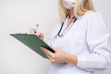 Kadın doktor portresi elinde reçeteyle ve yüzünde cerrahi maskeyle..