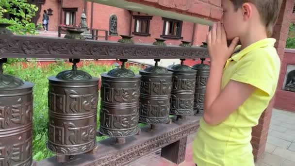 Vit pojke vidrör, roterande nepalesiska traditionella metall bönehjul med mantra Om Mani Padme Hum, det betyder O, juvelen i lotusen, hängande i rad — Stockvideo