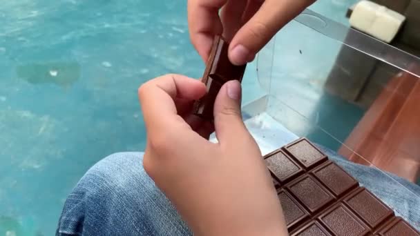 As mãos de uma criança quebrando uma barra de chocolate em pedaços e dando uma peça para uma câmera — Vídeo de Stock