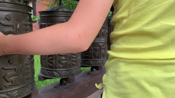 Caucasian boy touching, rotating nepalese traditional metal prayer wheels with mantra Om Mani Padme Hum, that means O, the jewel in the lotus, hanging in a row — Stock Video