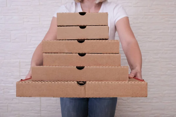 Woman holding many pizza boxes of different sizes.