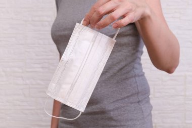 Beyaz cerrahi maske tutan kadın, elinde yüz maskesi ile virüslere, bakterilere, mikroplara, koronavirüs koruma konseptine karşı kişisel koruma ekipmanlarını gösteriyor..