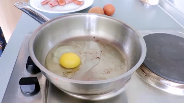 Náčelník rozbíjí kuřecí vejce a smaží je na kovové pánvi v kuchyni. — Stock video