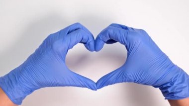 Tıbbi eldivenli bir doktorun ya da hemşirenin elleri beyaz bir arka planda, ilgili bir doktor ve tıp konseptinde bir kalp tasvir eder..