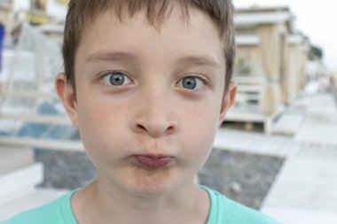 Başarısız bir yaz tatili konsepti, umutsuz bir portre, sahilde komik suratlı üzgün bir çocuk, deniz kıyısındaki tatil beldesi.