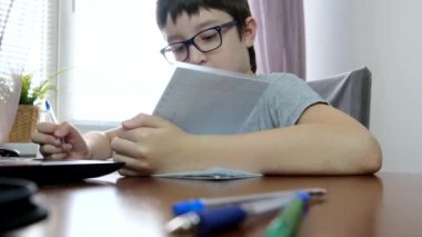 Bir çocuk, okul çocuğu masada dizüstü bilgisayarla oturuyor ve evde ödev yapıyor, e-öğreniyor, uzaktan ders veriyor ve online eğitim kavramını uyguluyor.