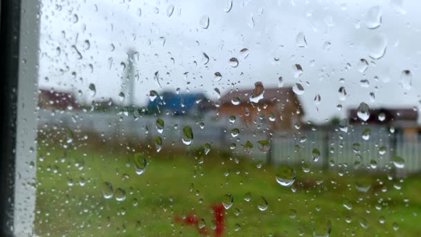 Капли дождя стекают по стеклу окна загородного дома, летом дождь, пасмурное серое небо, грусть и одиночество — стоковое видео