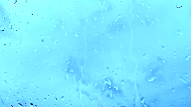 Regndroppar droppar, faller ner i det blå fönstret glas — Stockvideo